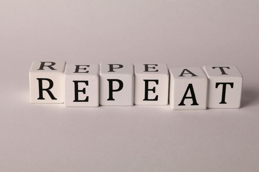 Wooden blocks arranged to spell 'REPEAT' on a neutral background.