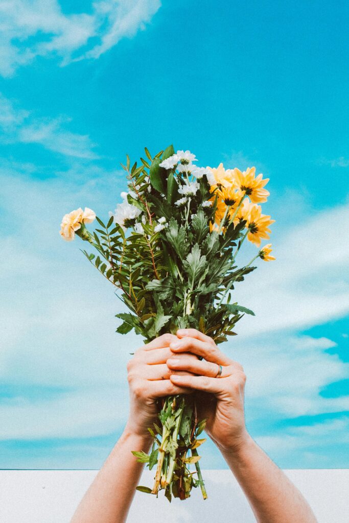 Hands holding a colorful flower bouquet beneath a vivid spring sky, symbolizing renewal.