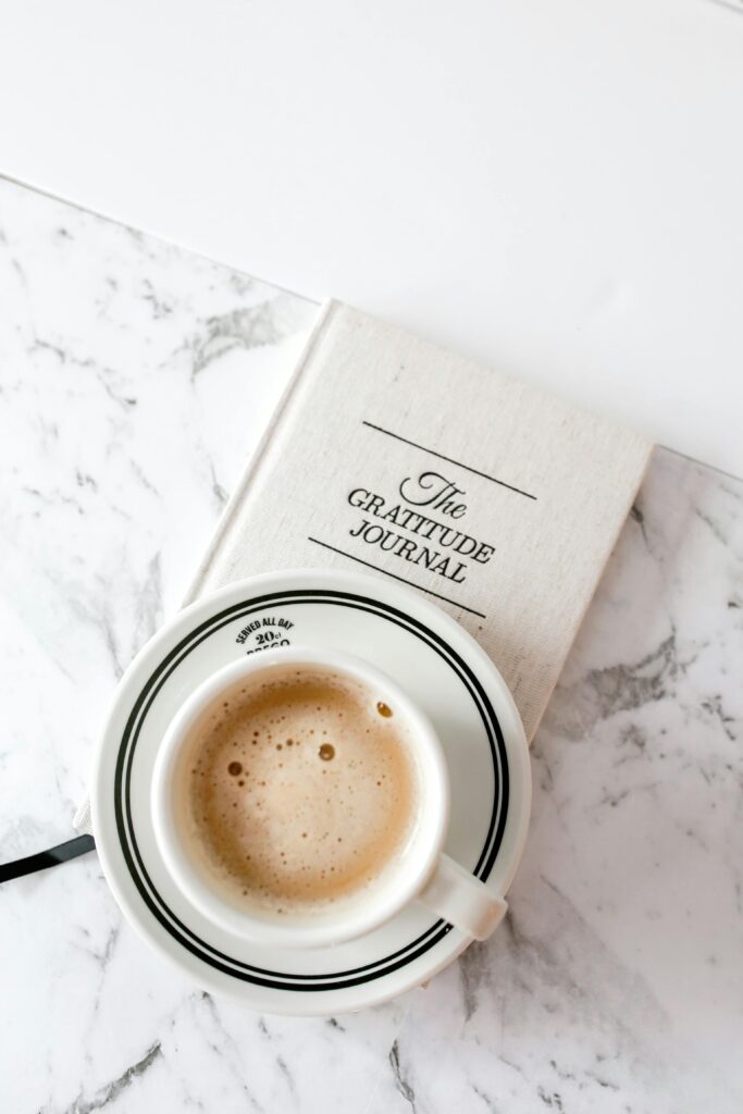 A cup of coffee rests on a gratitude journal against a marble backdrop, capturing peaceful moments.