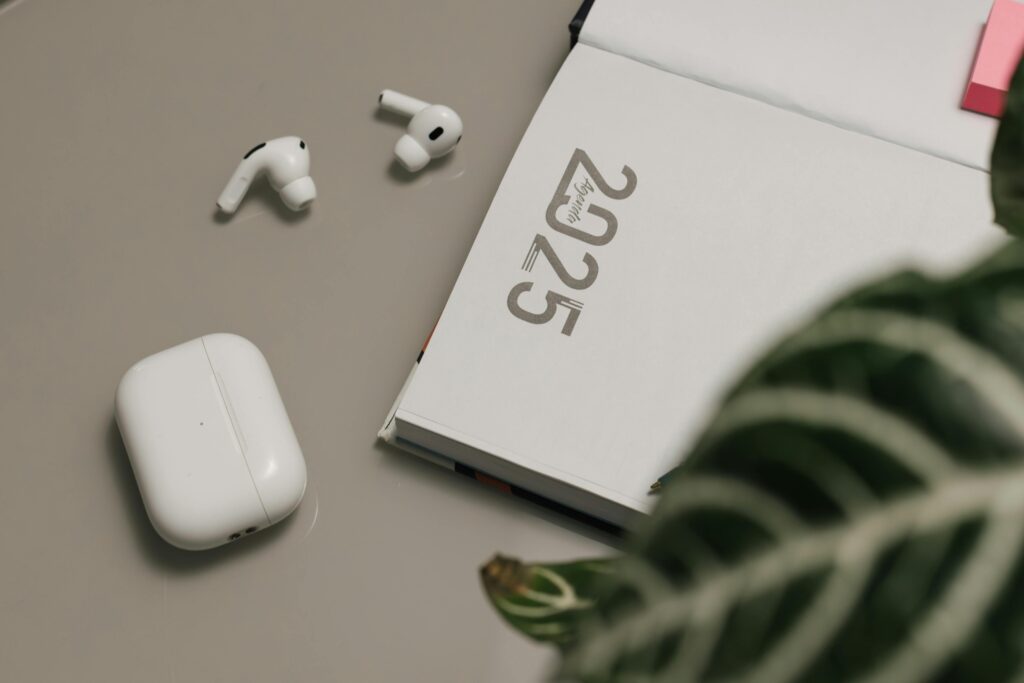 Stylish desk setup with a 2025 notebook, wireless earbuds, and a plant for a modern workspace.