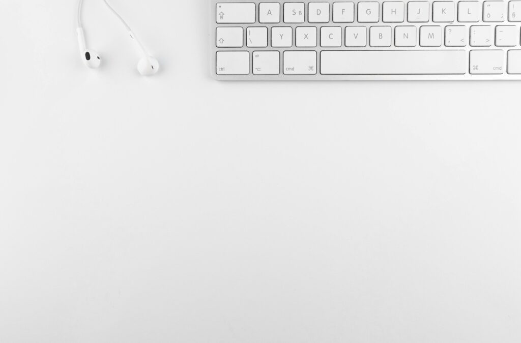 Top view of a white minimalist desk featuring a keyboard and earphones, ideal for technology themes.