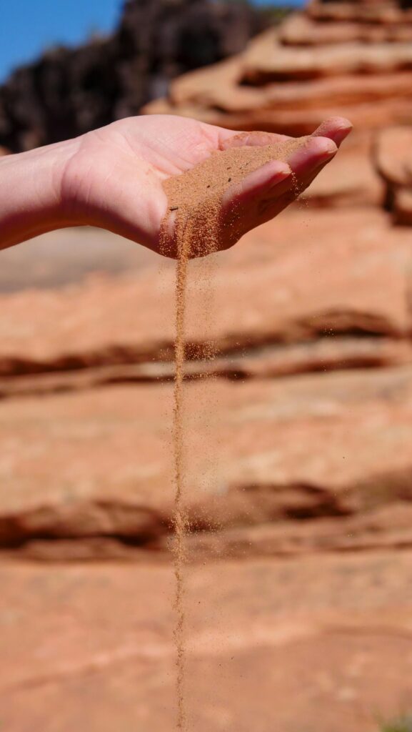 Close-up of a hand letting brown sand slip through fingers, captured outdoors.